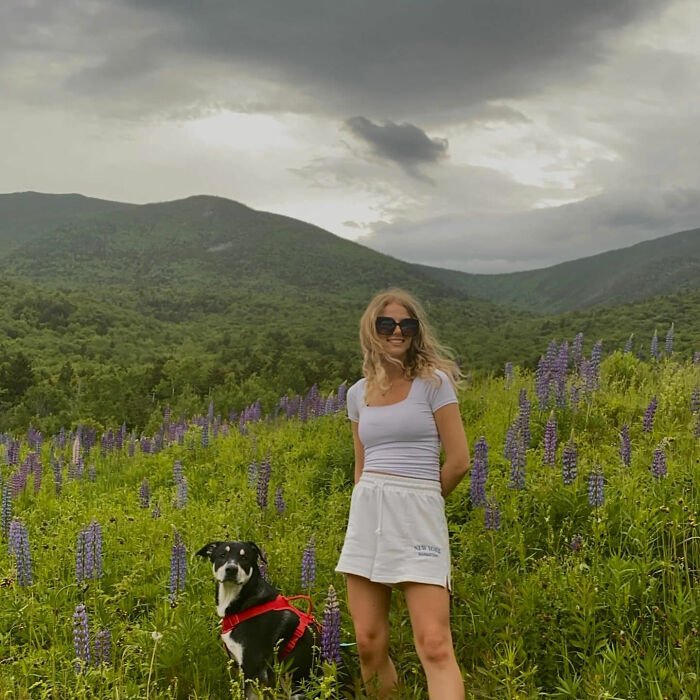 Young woman hiking New York's highest peak with her dog in wildflowers under cloudy sky.