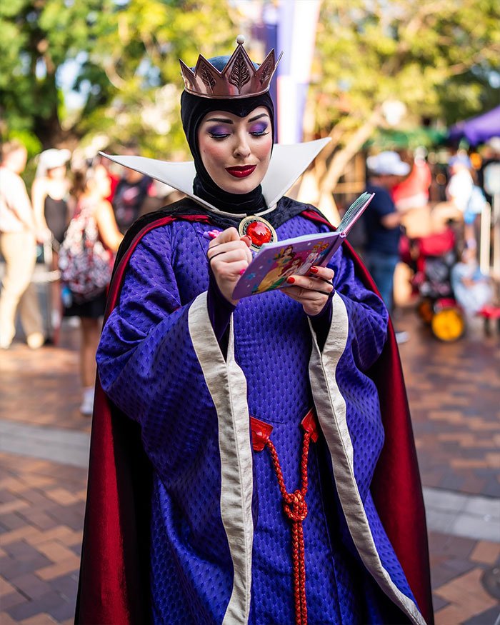 Actress in Disneyland Evil Queen costume signing autograph, representing ex-Disneyland Evil Queen sharing truth behind firing.