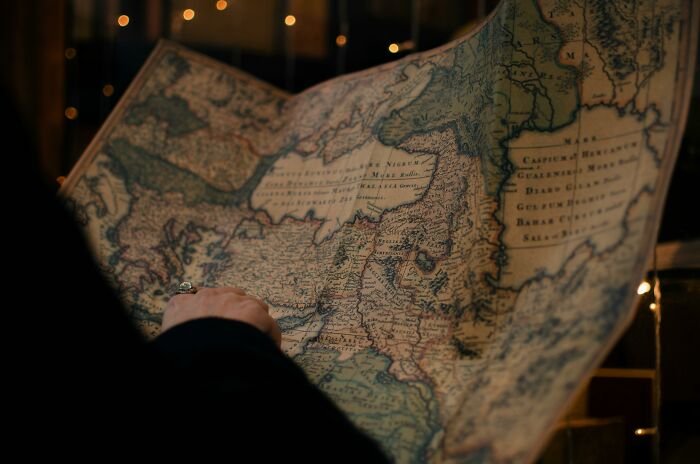 Person holding and examining an antique world map featuring Afghanistan among 30 countries to identify on the map.