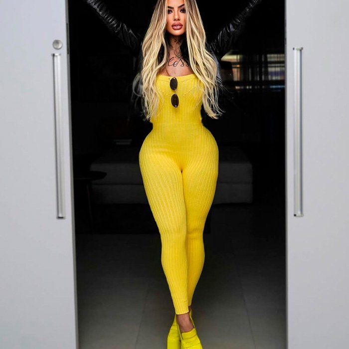 Woman influencer in a yellow outfit posing confidently indoors, highlighting glamorous style and femininity after major plastic surgery.