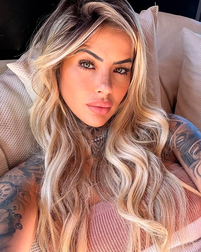 Glamorous influencer with long blonde hair and tattoos posing indoors, reflecting on plastic surgery complications risks.