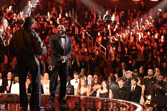 Grammy seatfiller in tuxedo on stage with large audience watching during a prestigious music awards event.