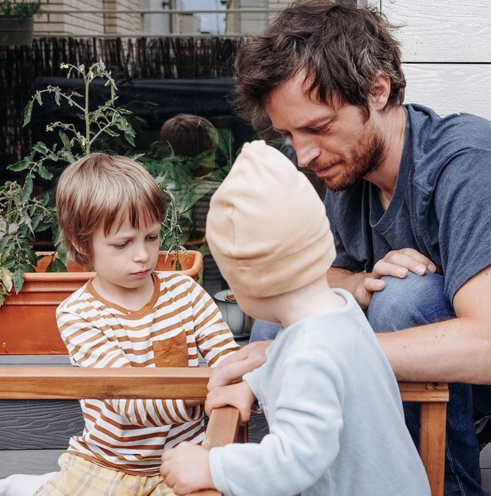Man warns couple about having kids while forgetting how many children he has, seen interacting with two young children outdoors.