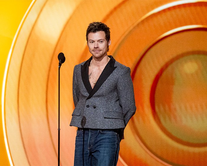Harry Styles on stage at the 2026 Grammys wearing a gray blazer and jeans, sparking outfit criticism.