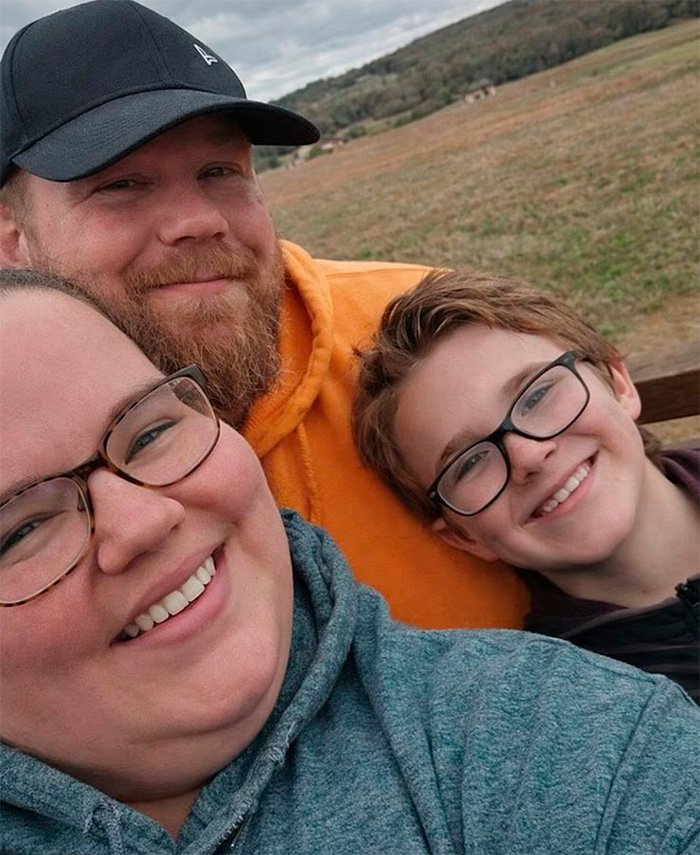 Heartbroken mom with adoptive father and 11-year-old child smiling outdoors in a rural setting.