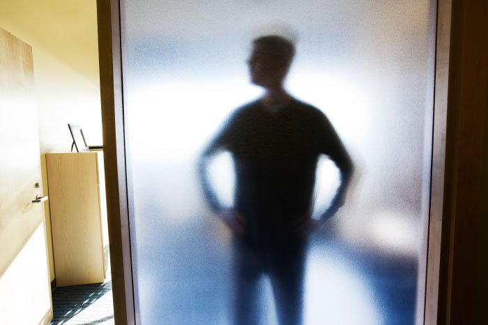 Silhouetted man standing behind frosted glass, representing creepy dad trying to lie and landing in jail.