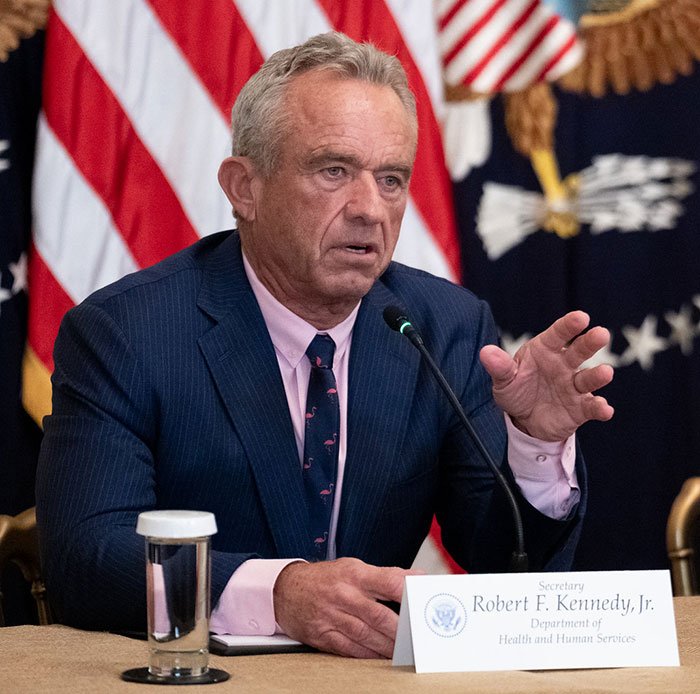 Robert F Kennedy Jr. speaking at a podium with U.S. flags behind him, related to his new workout video madness.
