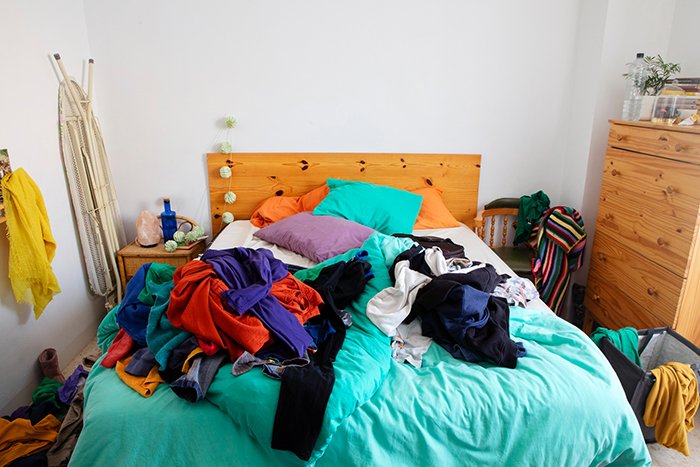 A cluttered bedroom with unwashed clothes scattered on the bed, illustrating concerns over new parents’ home condition before CPS involvement.