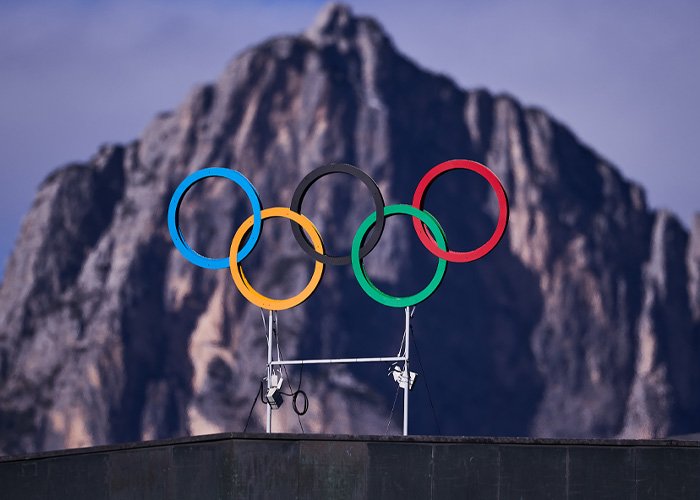 Olympic rings displayed against mountain backdrop highlighting controversy over misgendering incident involving trans Olympian.