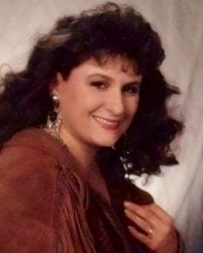 Mom of three from North Carolina smiling with dark curly hair, wearing earrings and a brown top in a close-up portrait.
