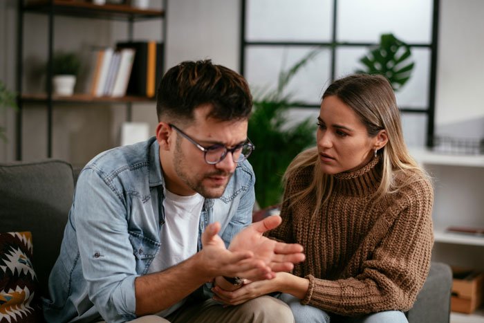 Man and woman having a serious conversation in a living room about moving in and apartment ownership issues.