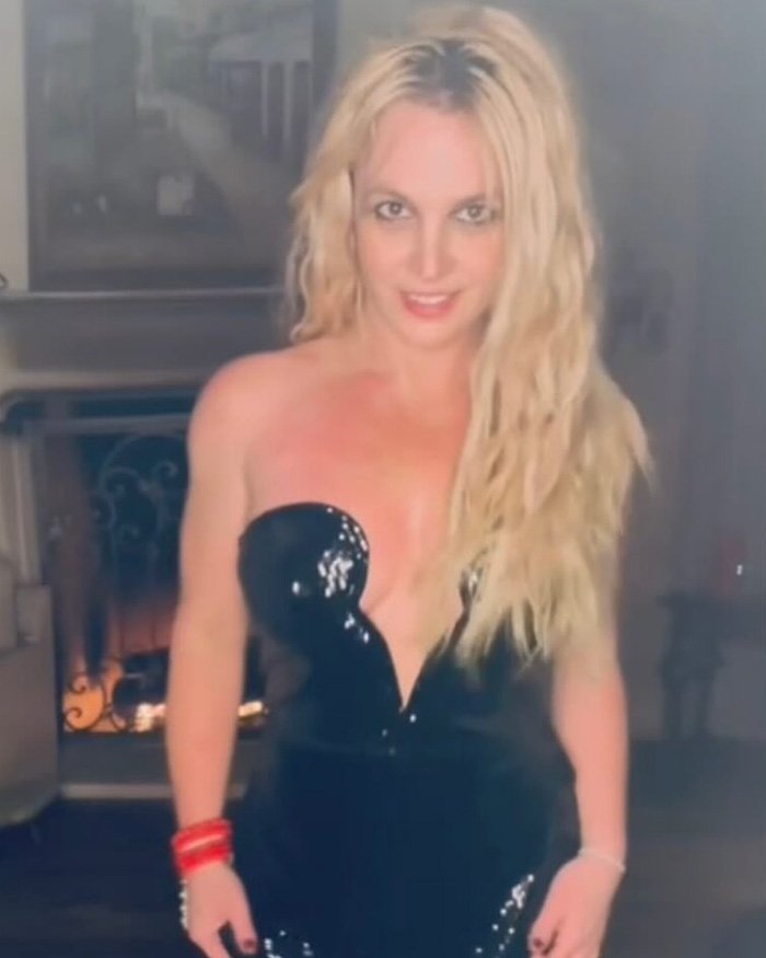 Britney Spears revealing bra and dancing in a shiny black outfit, showcasing a crop top style and confident pose indoors.