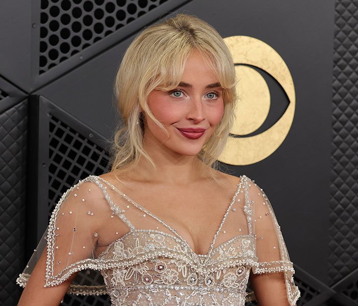 Sabrina Carpenter posing at an event, wearing a sheer beaded dress, amid controversy over her 2026 Grammys performance.