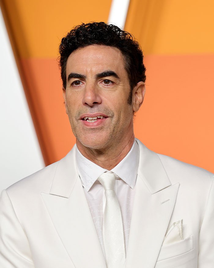 Sacha Baron Cohen in a white suit at a public event, breaking silence with rare message to ex‑wife after divorce