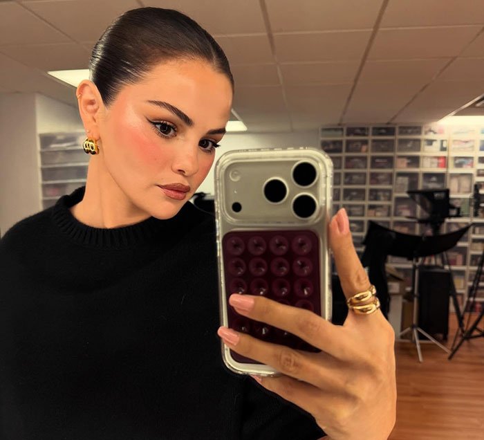 Selena Gomez taking a selfie, showcasing her makeup and hairstyle, sparking swimsuit debate after fans notice odd detail.