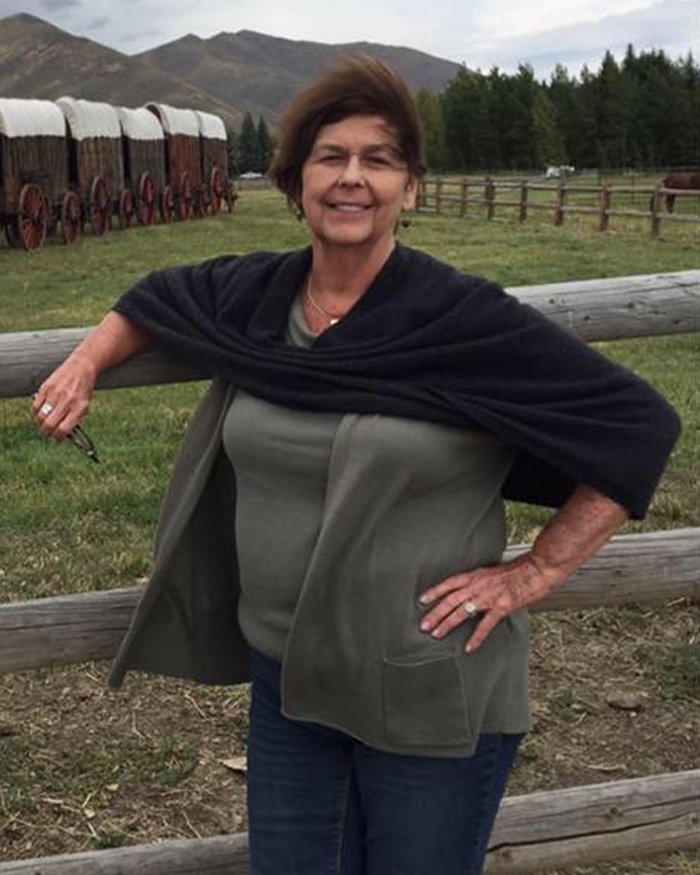 Woman standing outdoors near a wooden fence with covered wagons and mountains in the background, referencing ransomware Bitcoin demand.