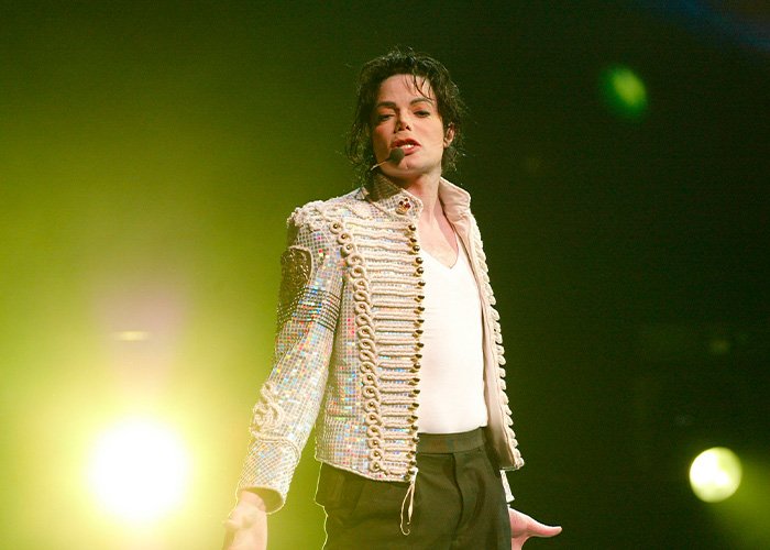 Michael Jackson performing on stage wearing a sequined military jacket with lighting highlighting his presence.