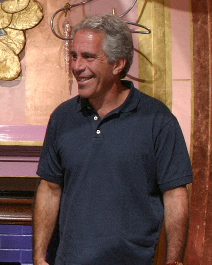 Man with gray hair in a navy polo shirt smiling indoors, related to viral theory Epstein may still be alive Fortnite connection.