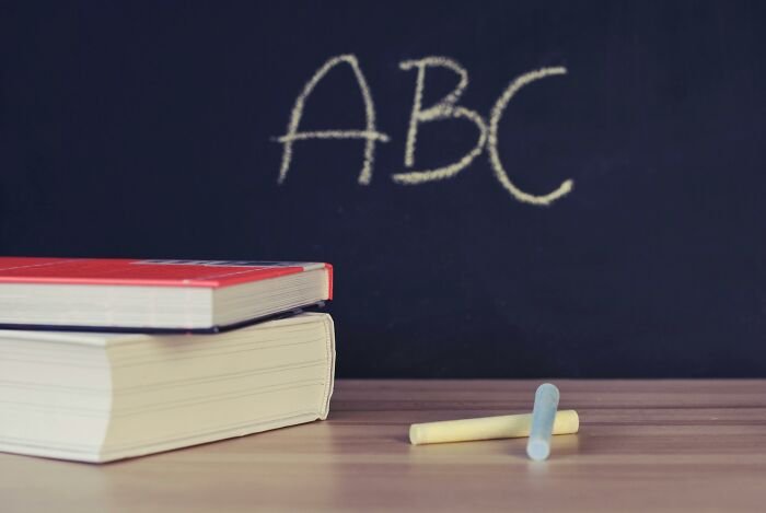 Stack of school books on desk with chalk sticks and ABC written on blackboard, related to school questions and A-student quiz.