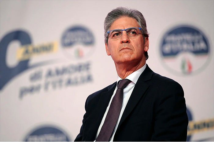 Man in suit and glasses appearing serious at a public event related to Winter Olympics host controversy.