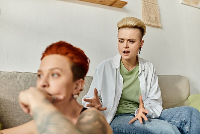 Two women in a tense conversation on a couch, reflecting the stress of taking care of wife's grandma and her will issues.