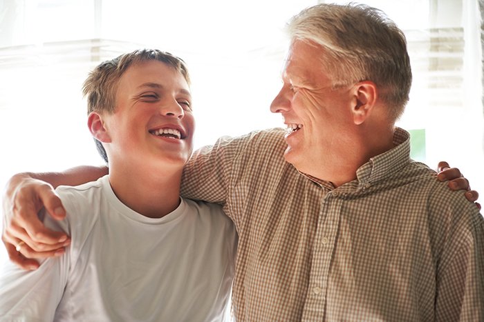 Middle-aged man and teenage boy smiling and embracing, illustrating family dynamics with boyfriend&rsquo;s son at home.