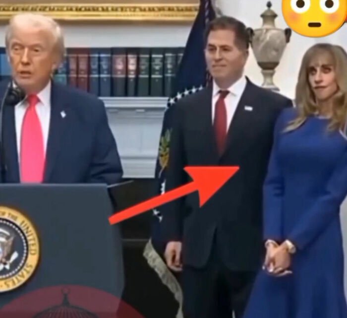 Woman displaying strange behavior standing next to man during White House press conference with presidential seal visible.