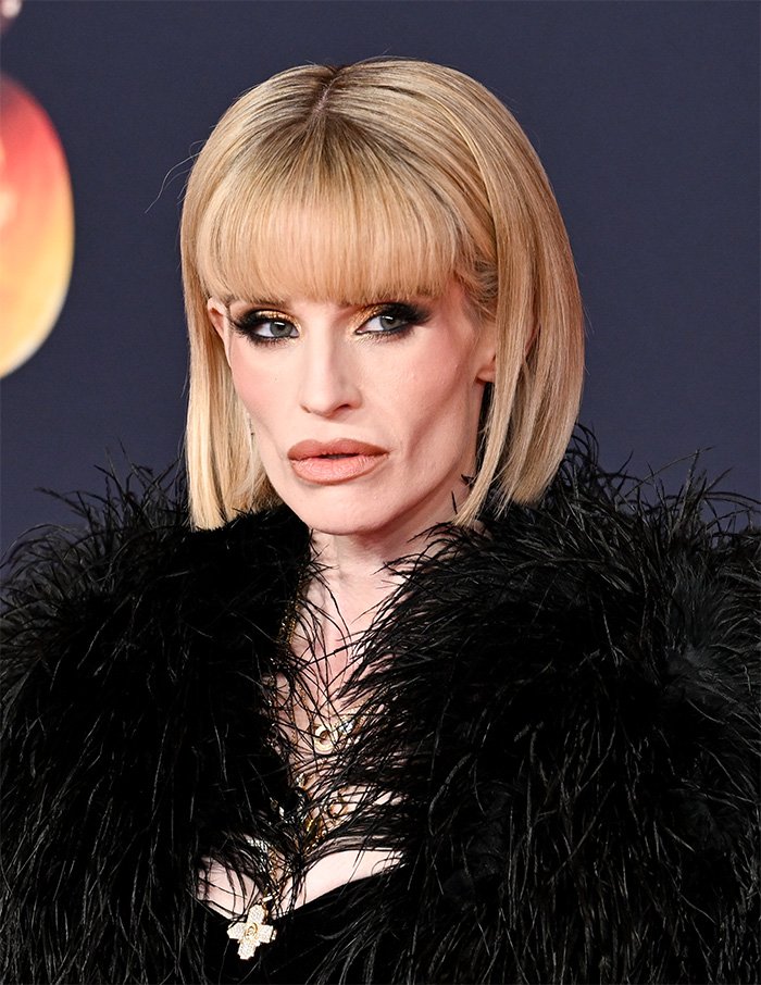 Kelly Osbourne with blonde bob hairstyle and black feathered outfit at a public event, sparking buccal fat removal rumors.