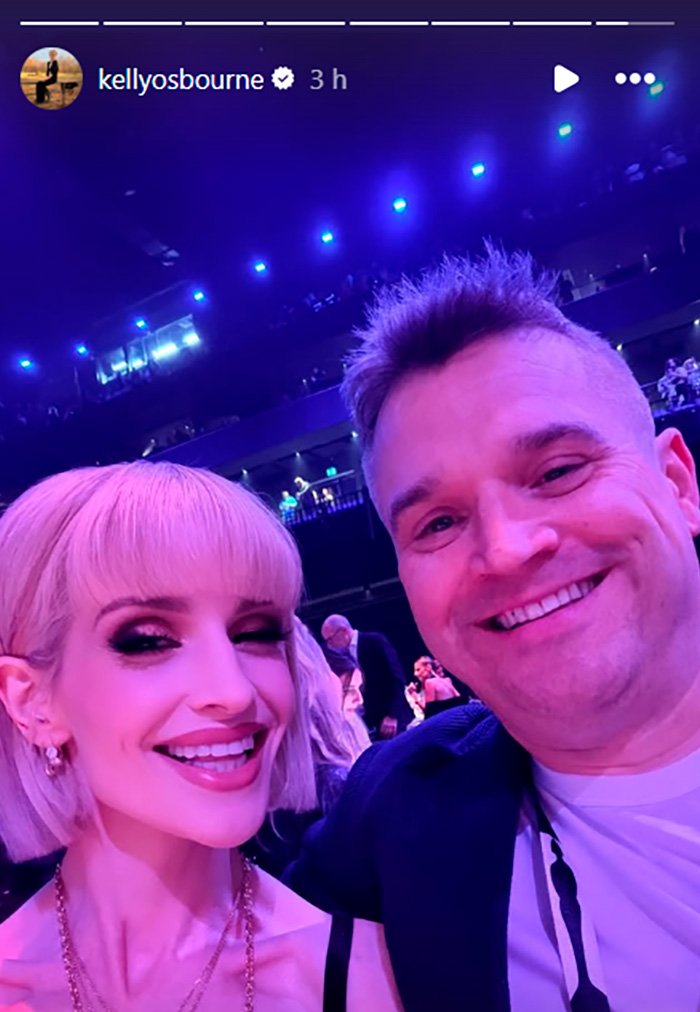 Kelly Osbourne and a man smiling in a brightly lit venue, fans speculate about buccal fat removal after Brit Awards appearance.