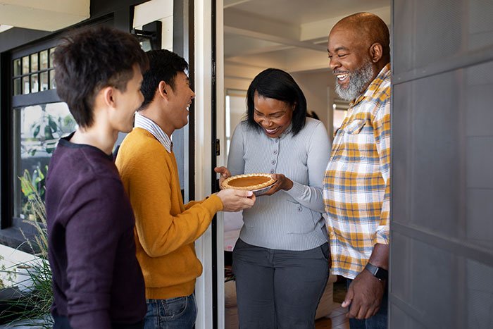 Group of neighbors happily sharing a pie at the doorstep, contrasting with a man stressed and paranoid about his neighbor.