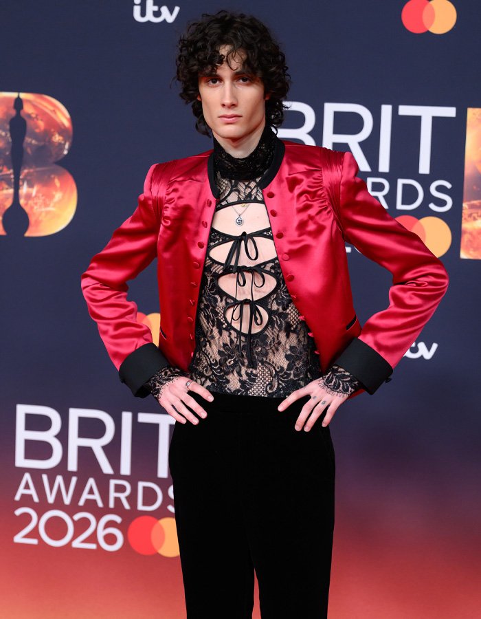 Singer at Brit Awards red carpet event wearing a red jacket and lace top amidst chaos during viral stage incident.